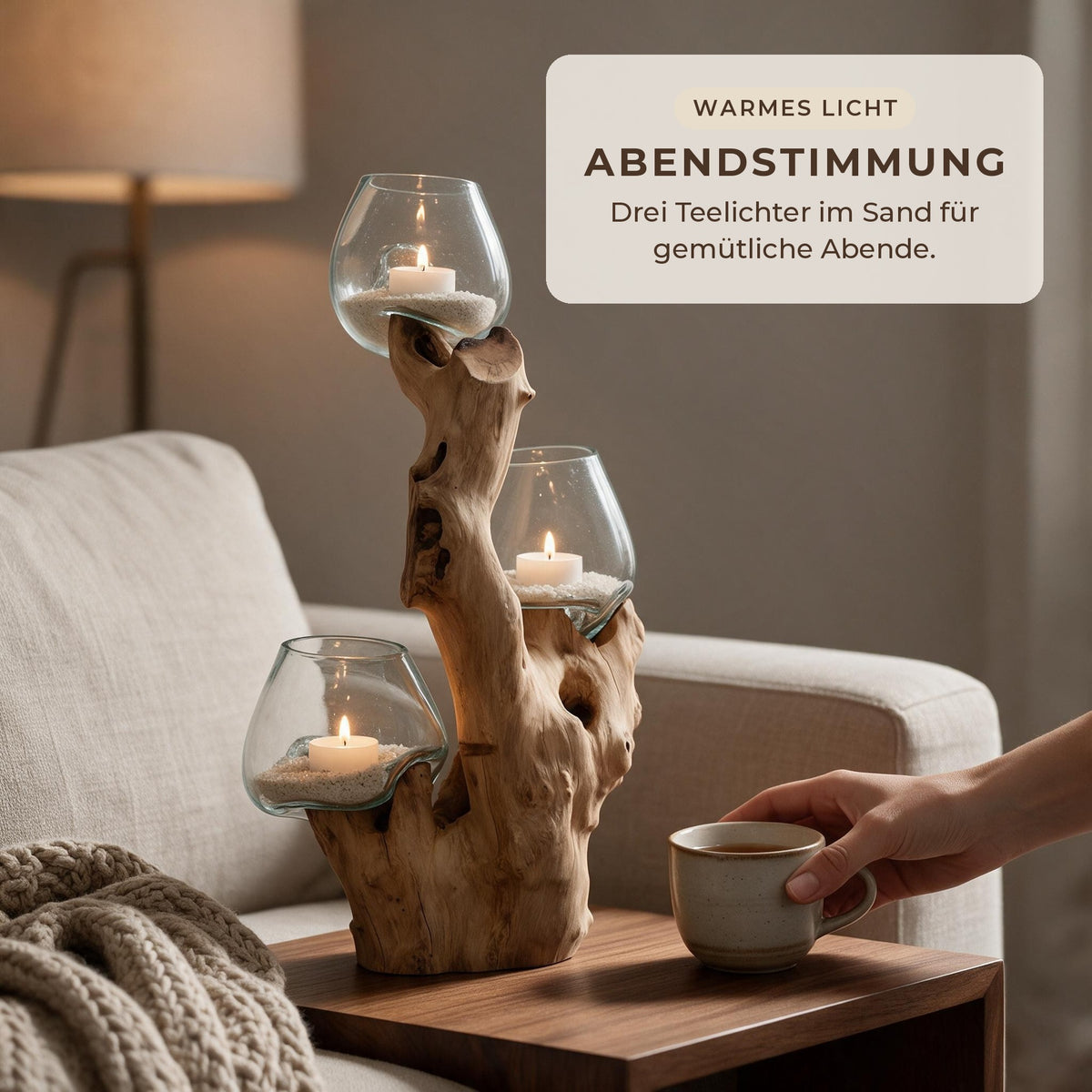 Wurzelholz-Windlicht mit drei brennenden Teelichtern im Sand auf einem Beistelltisch neben dem Sofa am Abend