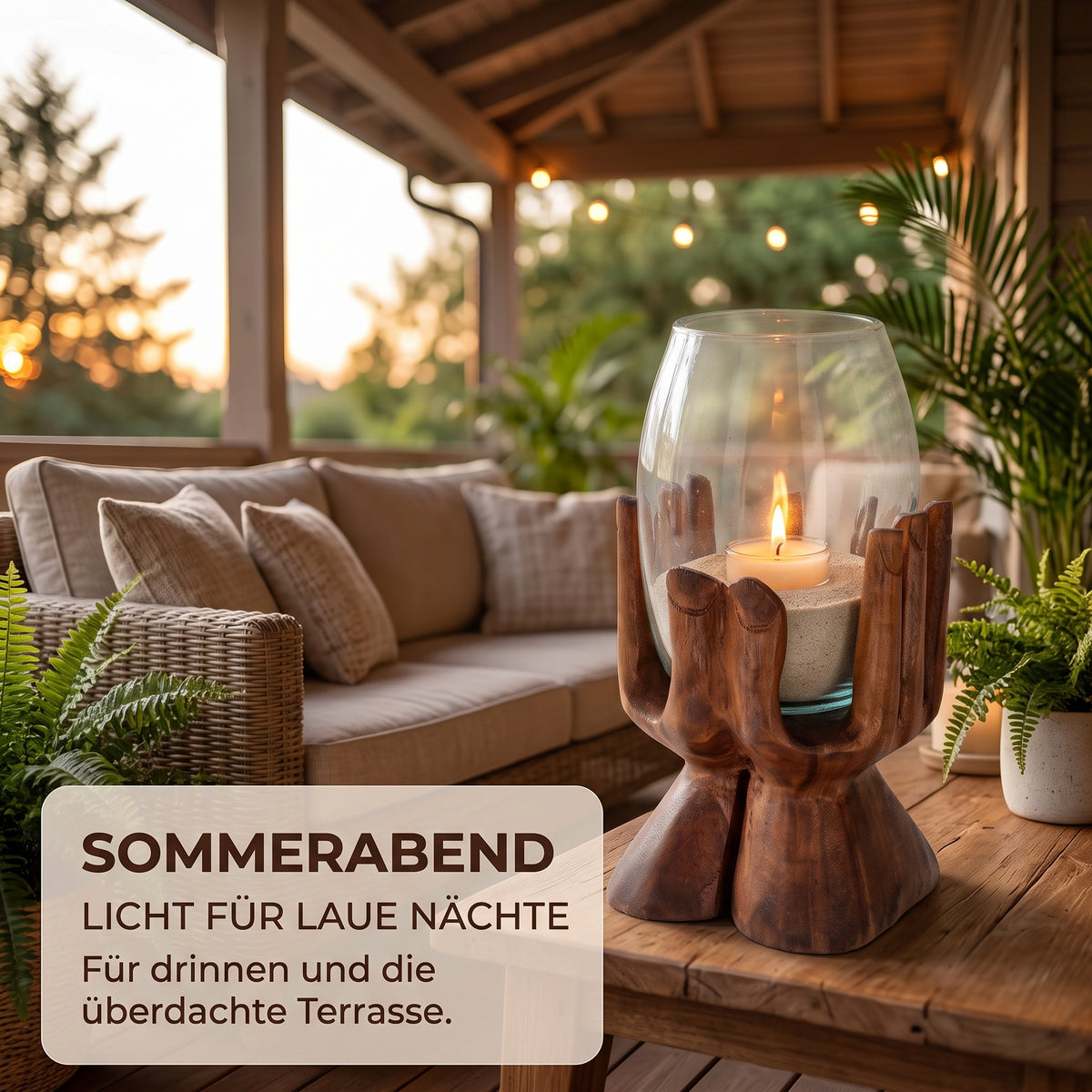 Holzhand mit Glas und brennender Kerze auf der überdachten Terrasse am Abend, als Windlicht für drinnen und den geschützten Außenbereich.